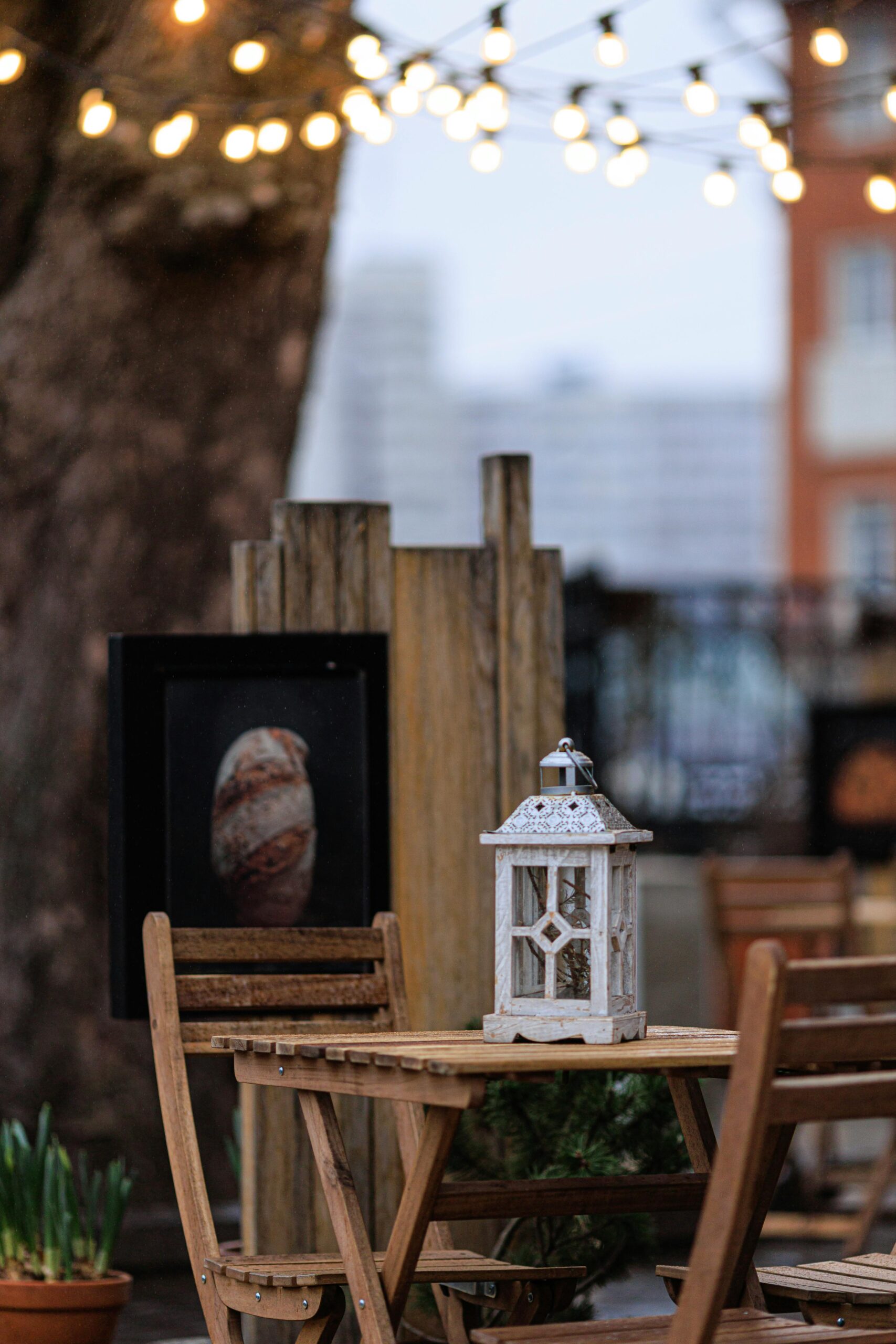 Charming outdoor patio with a rustic wooden table, chairs, and a decorative lantern under string lights.