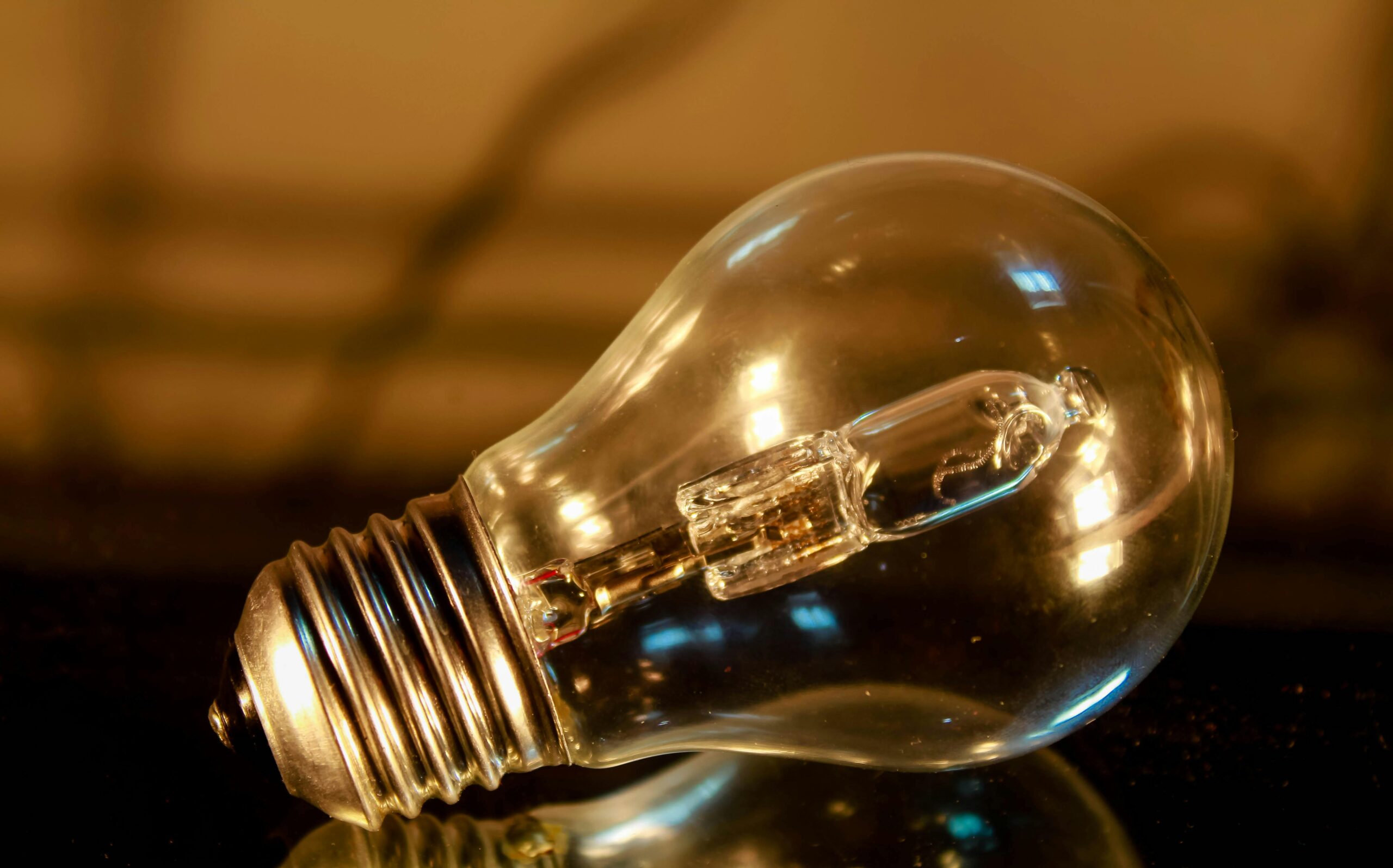Detailed macro shot of a clear incandescent light bulb reflecting on a surface.